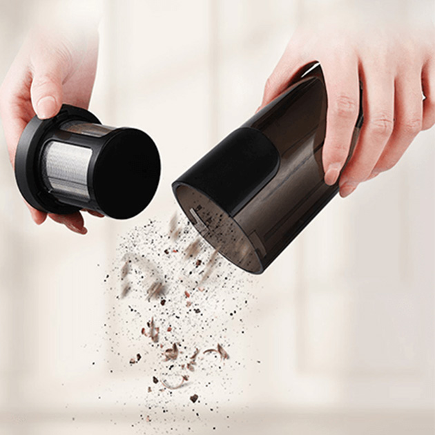 Una persona está sacudiendo el recipiente colector de suciedad para limpiar la aspiradora.